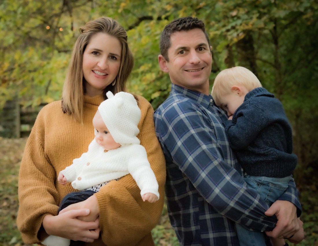 The mother and father look into the camera as the mother holds her daughter who looks to the side and the father holds his son who buries his head in his dad's chest.